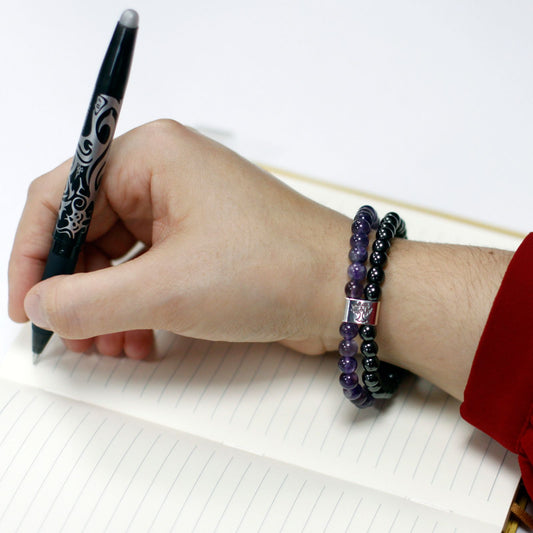 Hand holding a pen with a beaded bracelet on a white background