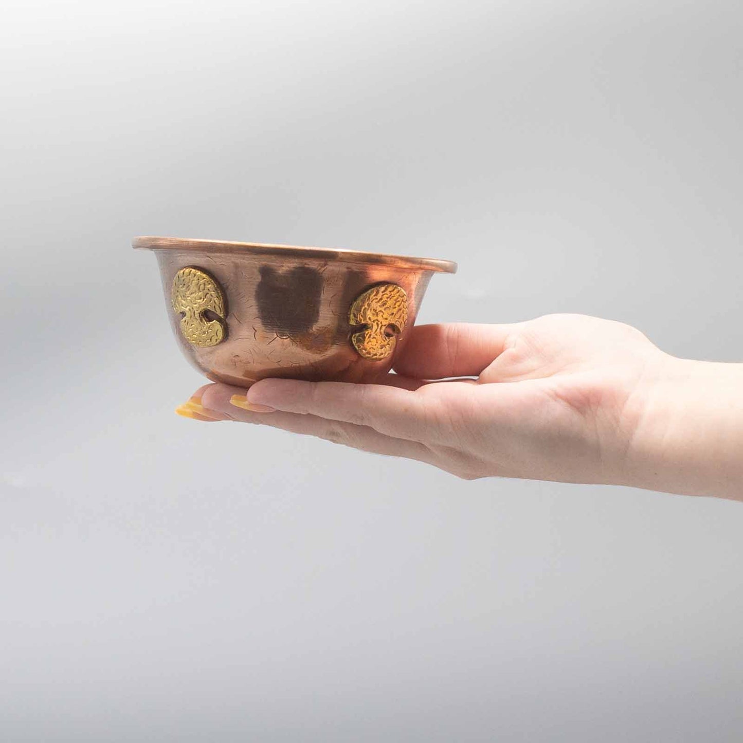 Hand holding a small copper bowl with gold accents against a plain background