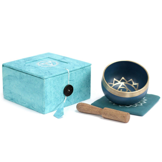 Blue singing bowl with gold interior, wooden stick, and turquoise box on a white background