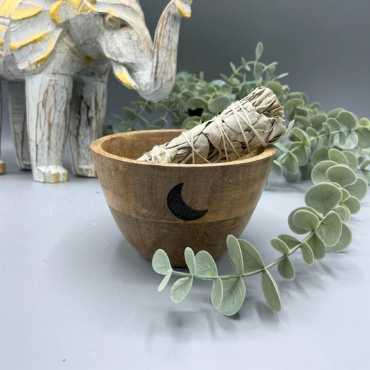 Wooden bowl with sage inside, surrounded by eucalyptus leaves and a stone elephant figurine.