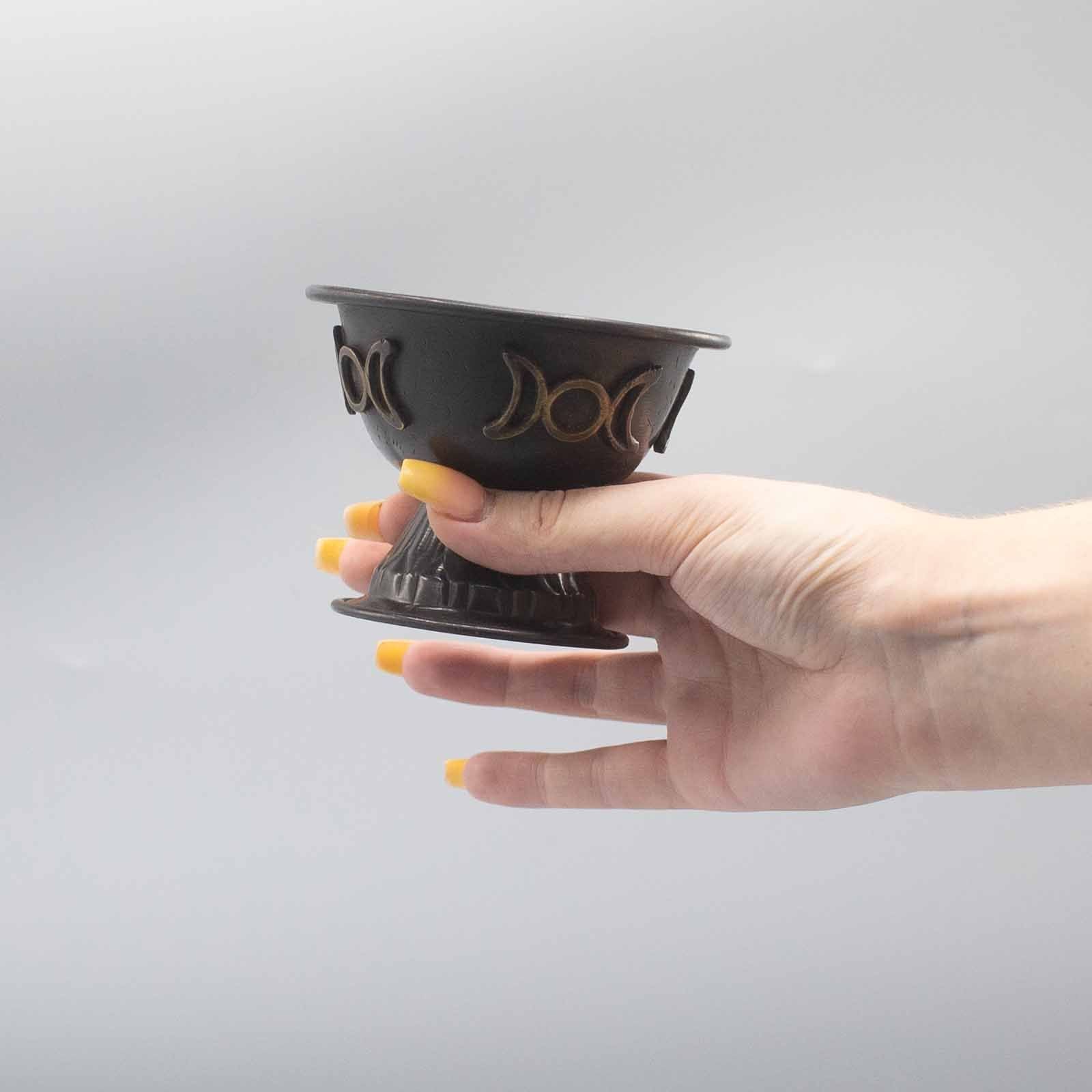 Hand holding a black decorative bowl with gold accents against a gray background